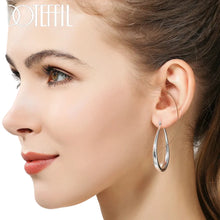 Close-up of a woman wearing silver hoop earrings with branding.