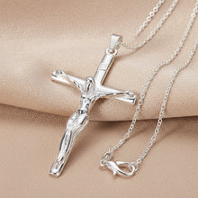 Silver crucifix necklace on a turquoise and beige background with 'Doteffil' branding.