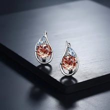 Pair of earrings with orange gemstones on a reflective surface, branded 'ATTA GEMS'.