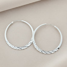 Silver hoop earrings on a textured surface with a purple fabric background