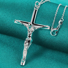 Silver crucifix pendant necklace on a teal fabric background with 'Doteffil' branding.