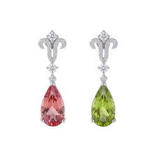 Two teardrop-shaped drop earrings with silver-toned metal settings and clear stones, one in pink and one in green, displayed on white cylindrical forms with the text 'ATTAGEMS' and 'STONE COLOR CHANGES WHILE LIGHT CHANGES'.