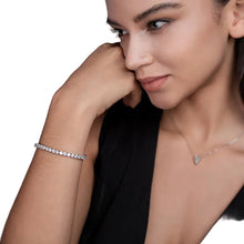 Woman wearing a silver bracelet and necklace with a gray background and '9' logo