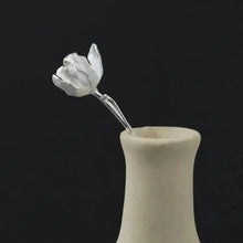 Decorative silver flower in a beige vase on a black.