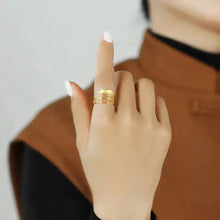 Hand wearing a gold ring with a blurred background and 'GEEZENCA' branding.
