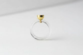 Clear glass ring with gold accent on a reflective surface, branded 