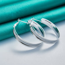Silver hoop earrings on a light blue fabric background with 'Doteffil' branding.