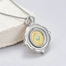 Silver necklace with a pendant featuring a gold emblem and turquoise stone on a white background.