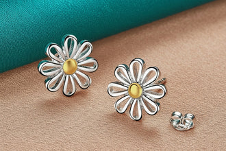 Silver flower-shaped earrings with a gold center on a teal fabric background