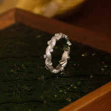 Silver ring with floral design on a textured surface, brand 'GEEZENCA' visible