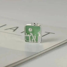 Silver pendant with green rectangular design on a reflective surface