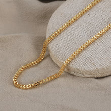 Gold chain on a textured beige surface with Orsa Jewels logo.