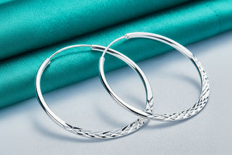 Silver hoop earrings on a light blue fabric background with 'DOKEFFIL' branding.