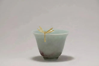 Green ceramic cup with a gold dragonfly decoration on a light gray background, featuring the brand 'GEEZENCA'.
