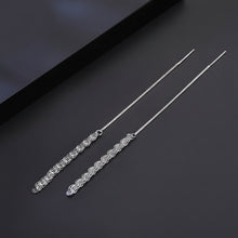 A pair of long silver-toned dangle earrings with intricate openwork filigree details, displayed on a dark textured surface next to a black box. The brand logo 'Orisa Jewels' is visible in the top left corner.