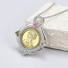 Jewelry pendant with gold coin and gemstones on a white surface, featuring the brand 'Geezenca'.