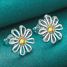 Silver flower-shaped earrings with gold centers on a teal fabric background, featuring the brand 'Doteffil'.