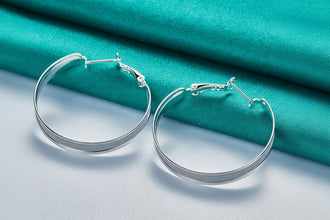 Silver hoop earrings on a teal fabric background with 'Doteffil' branding.
