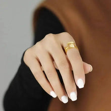 Hand wearing a gold ring with a blurred background and 'GEEZENCA' branding.