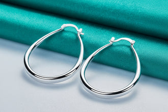 Silver hoop earrings on a teal fabric background with branding.