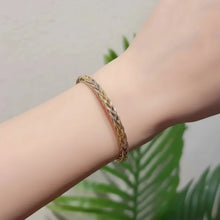 Gold bracelet on a wrist with a blurred green plant background, featuring the brand 'GEEZENCA'.