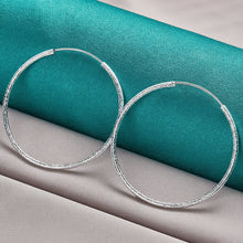 Silver hoop earrings with a measurement of 60mm on a teal and gray fabric background, featuring the brand 'Doteffil'.
