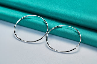 Silver hoop earrings on a teal fabric background with 'DOVEFFIL' branding.