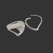 Silver heart-shaped earrings on a teal fabric background with 'Doteffil' branding.