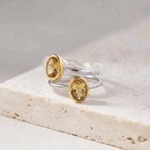 Gold ring with a yellow gemstone on a white stone surface, featuring the brand 'GEEZENCA'.