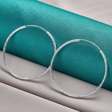 Silver hoop earrings on a teal and gray fabric background with Doteffil branding.