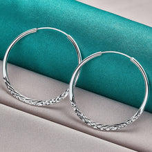 Silver hoop earrings on a teal and gray fabric background with 'Doteffil' branding.