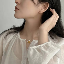 Woman wearing a necklace with a gold pendant, with 'GEEZENCA' branding.