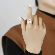 Hand wearing a ring with a building design, against a neutral background