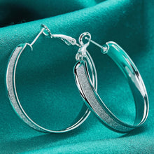 Silver hoop earrings on a teal fabric background with 'Doteffil' branding.