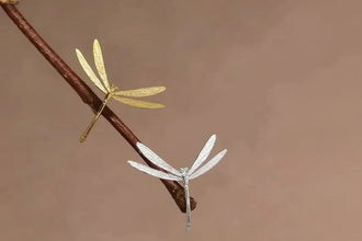 Gold and silver dragonfly-shaped earrings on a branch with 'GEEZENCA' branding.