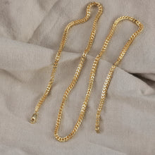Gold chain on a textured beige fabric background with 'Orsa Jewels' branding.