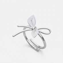 Silver bow-shaped ring with a heart detail on a white background, branded 'Geezenca'.