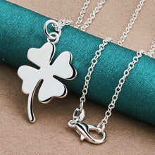 Silver four-leaf clover pendant necklace on a turquoise spool of thread.