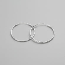 Silver hoop earrings with a measurement of 60mm on a teal and gray fabric background.