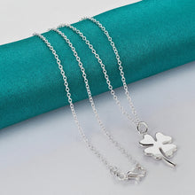 Silver necklace with a clover pendant on a teal fabric background