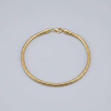 A gold snake chain bracelet with a lobster clasp, displayed on a black textured background with a brand logo in the top-left corner.