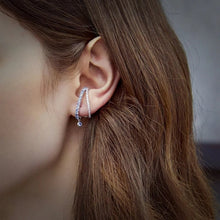 Close-up of an ear wearing a silver earring with 'Geezenca' branding.