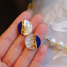 Close-up of a hand holding a pair of earrings with blue and gold design.