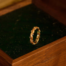 Gold ring with green gemstone on a black stone surface inside a wooden box, branded 'GEEZENCA'.