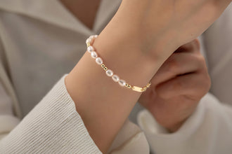 Pearl bracelet on a wrist with a blurred background, featuring Orsa Jewels logo.