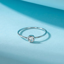 A silver-toned minimalist ring with a single round clear gemstone, displayed on a light blue background with a soft shadow. The brand logo 'Orua Jewels' is visible in the top-left corner.