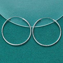 Silver hoop earrings on a teal background with Doteffil branding.