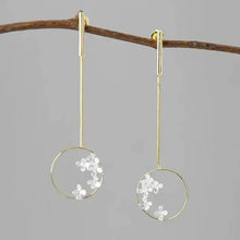 Gold earrings with floral elements hanging on a branch against a gray background