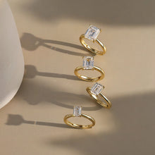 Four gold rings with rectangular clear gemstones arranged vertically on a beige surface with soft shadows. The Orsa Jewels logo is visible in the top-left corner.