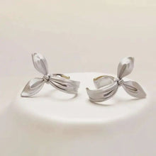 Silver bow-shaped earrings on a light beige background with 'GEEZENCA' branding.